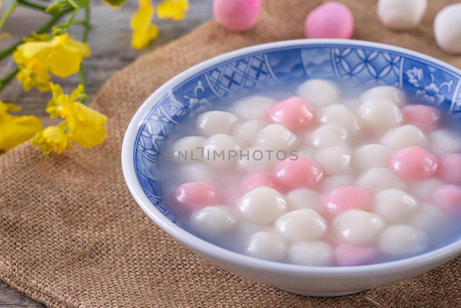 Close up of red and white tangyuan (tang yuan, glutinous rice dumpling balls) in blue bowl on wooden background for Winter solstice festival food.