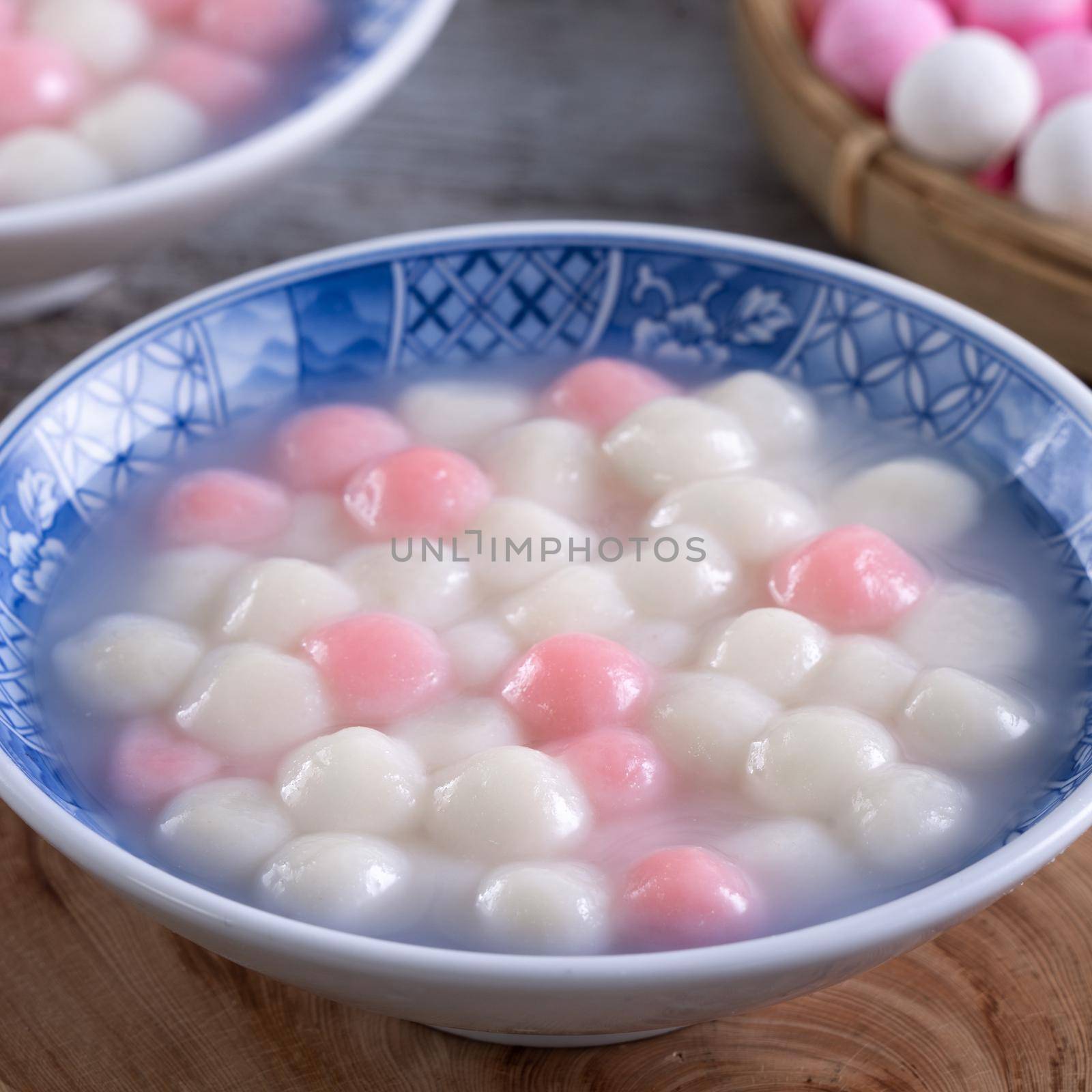 Close up of red and white tangyuan (tang yuan, glutinous rice dumpling balls) in blue bowl on wooden background for Winter solstice festival food.