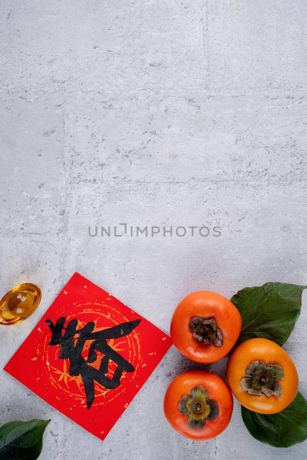 Top view of fresh sweet persimmons kaki with leaves on gray table background for Chinese lunar new year fruit design concept, the word means spring is coming.