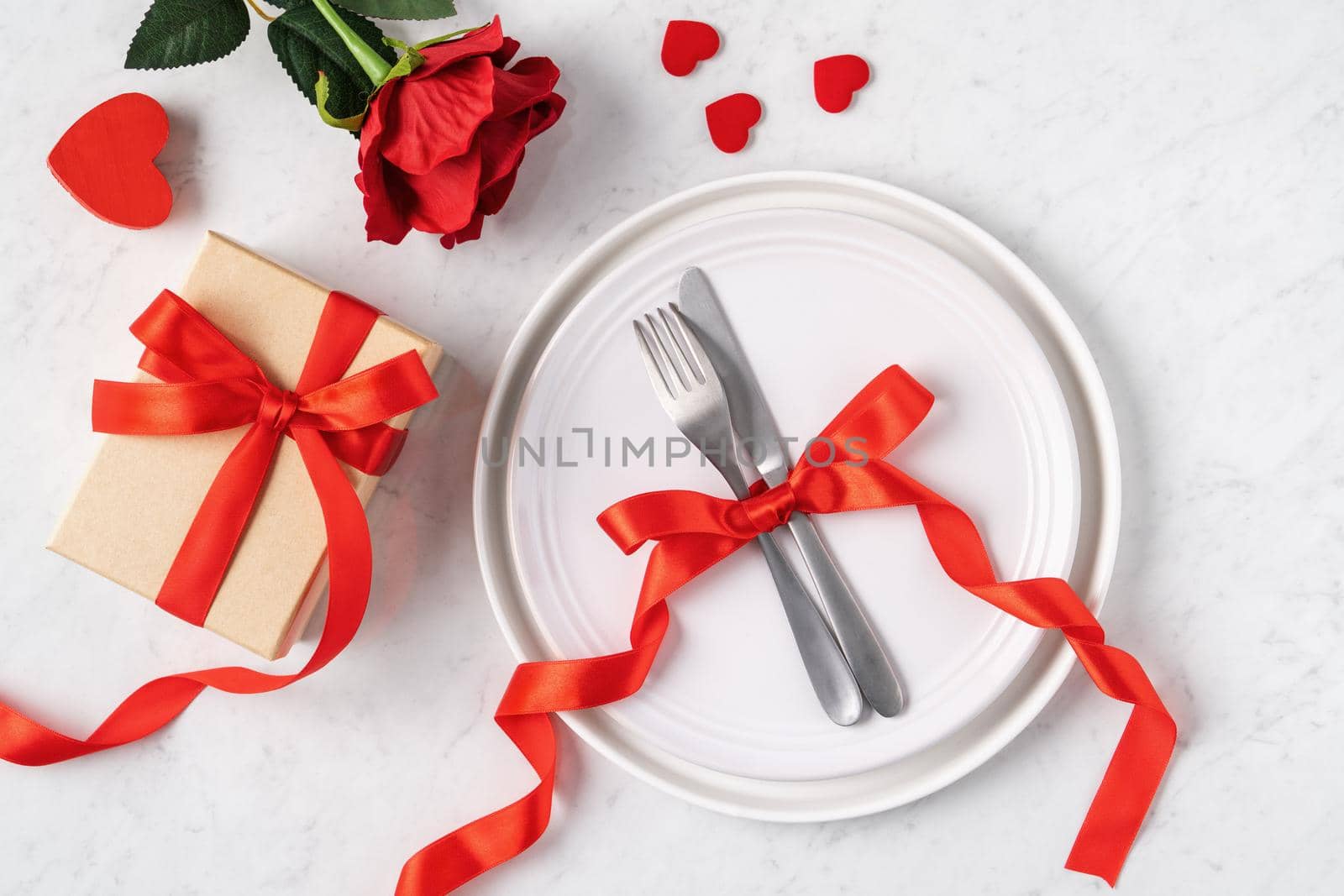 Empty white plate with tableware, ribbon, gift and roses for Valentine's Day special holiday dating meal concept.