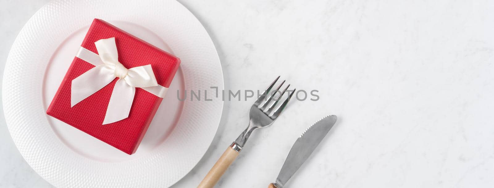 Empty white plate with tableware, ribbon, gift and roses for Valentine's Day special holiday dating meal concept.