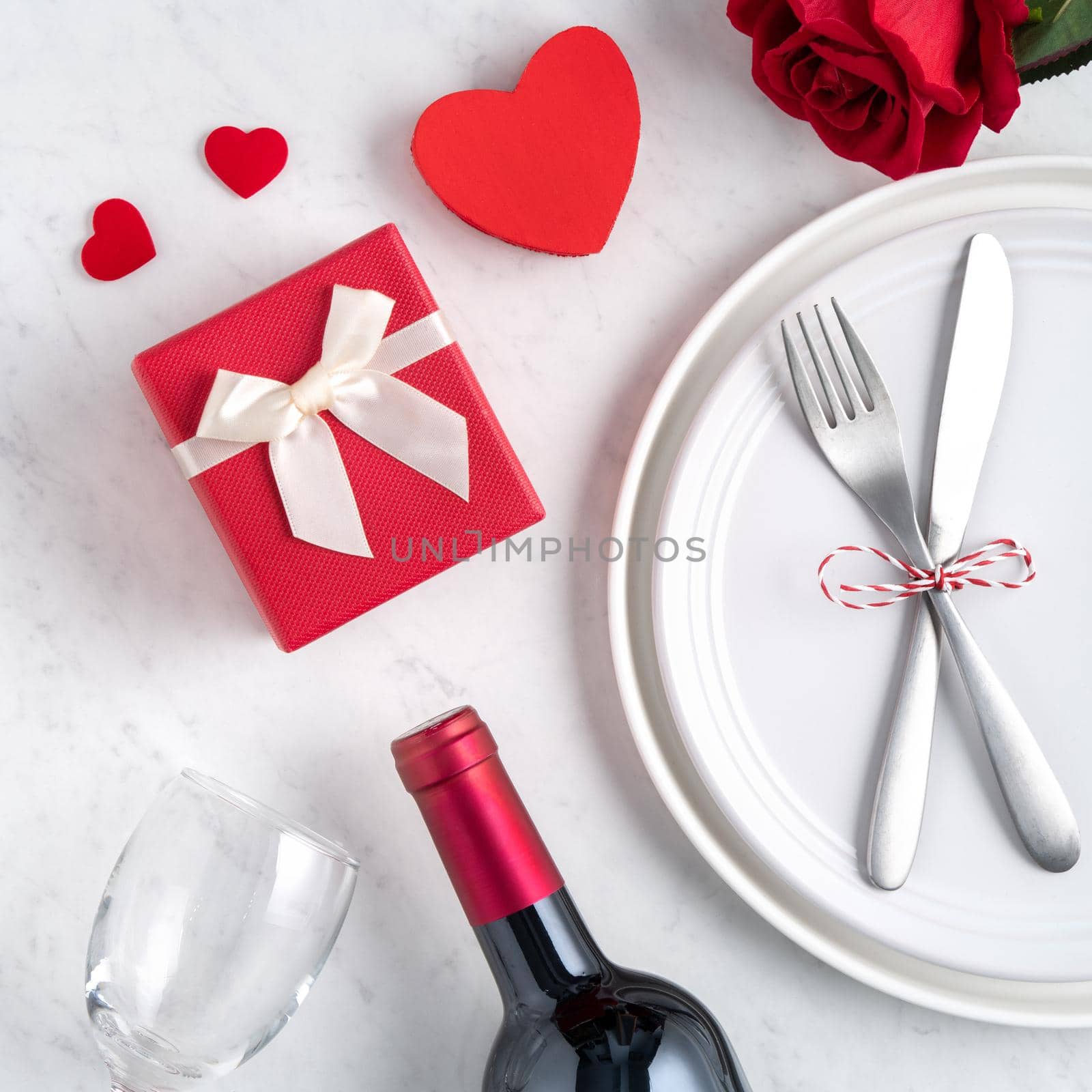 Empty white plate with tableware, ribbon, gift and roses for Valentine's Day special holiday dating meal concept.