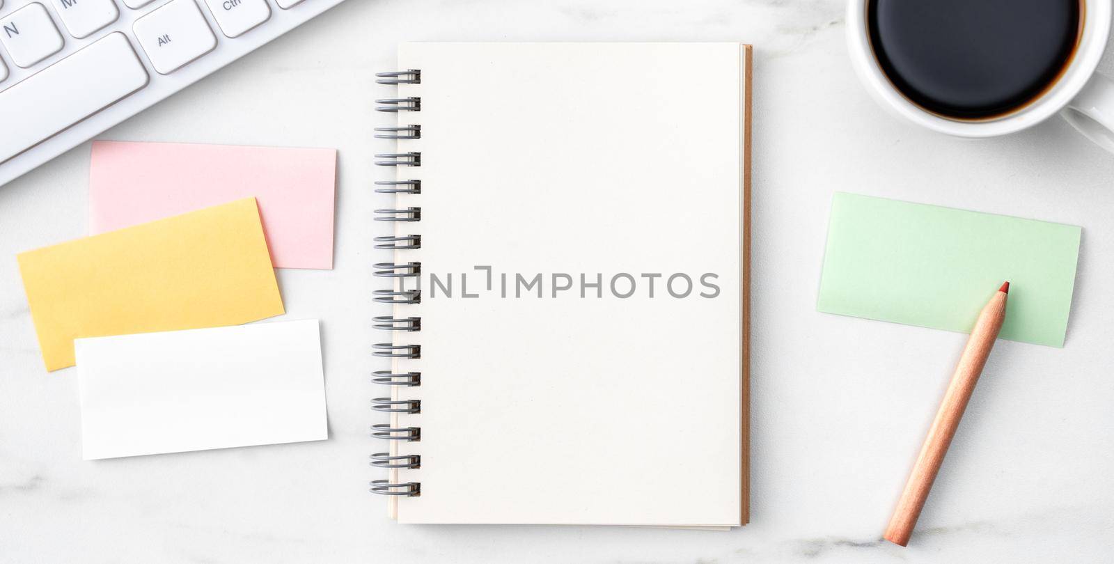Top view of office table desk cozy work concept with keyboard, notebook, pencil, eyeglasses and coffee on bright marble white background.