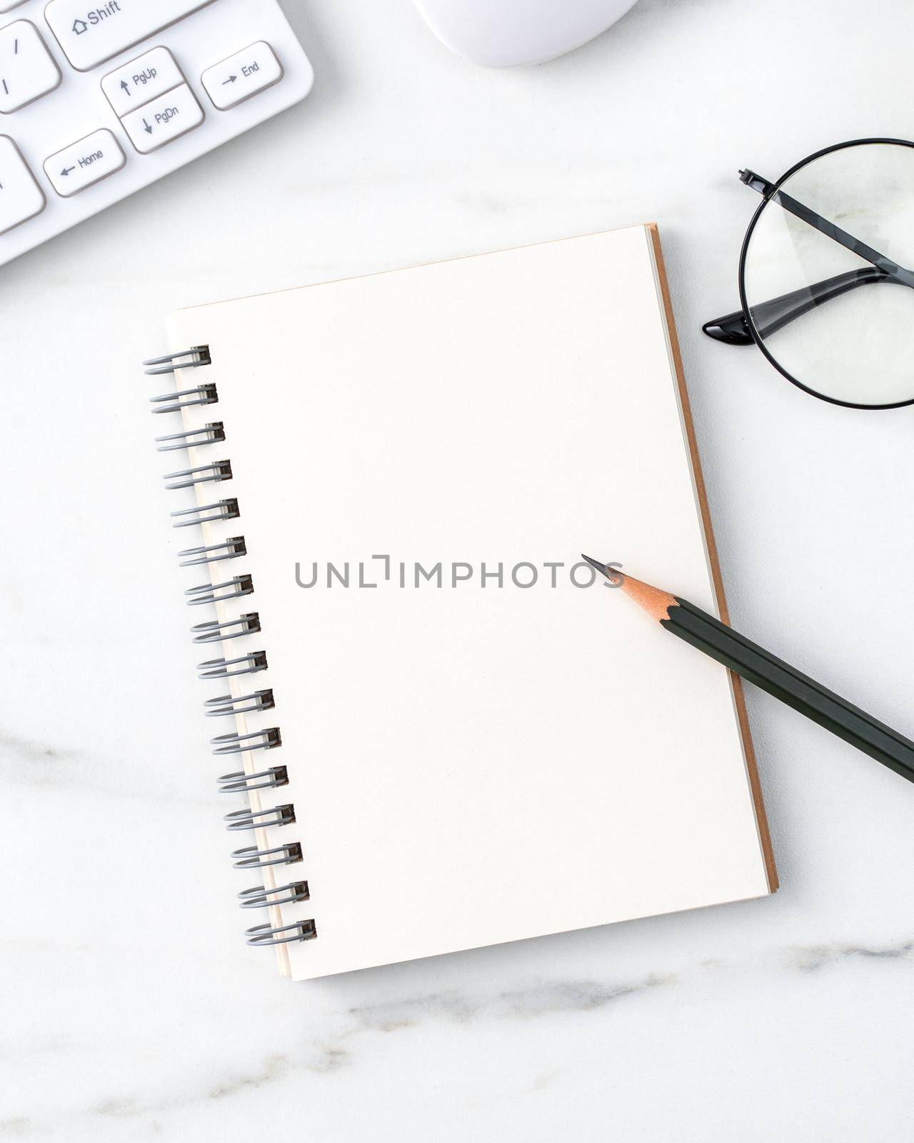 Top view of office table desk cozy work concept with keyboard, notebook, pencil, eyeglasses and coffee on bright marble white background.