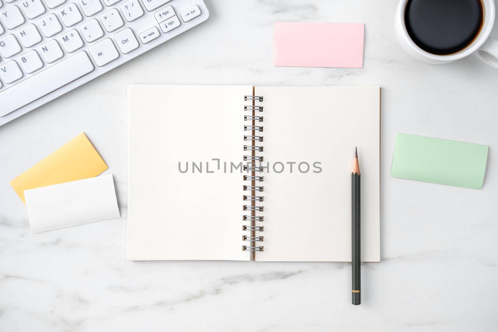 Top view of office table desk cozy work concept with keyboard, notebook, pencil, eyeglasses and coffee on bright marble white background.