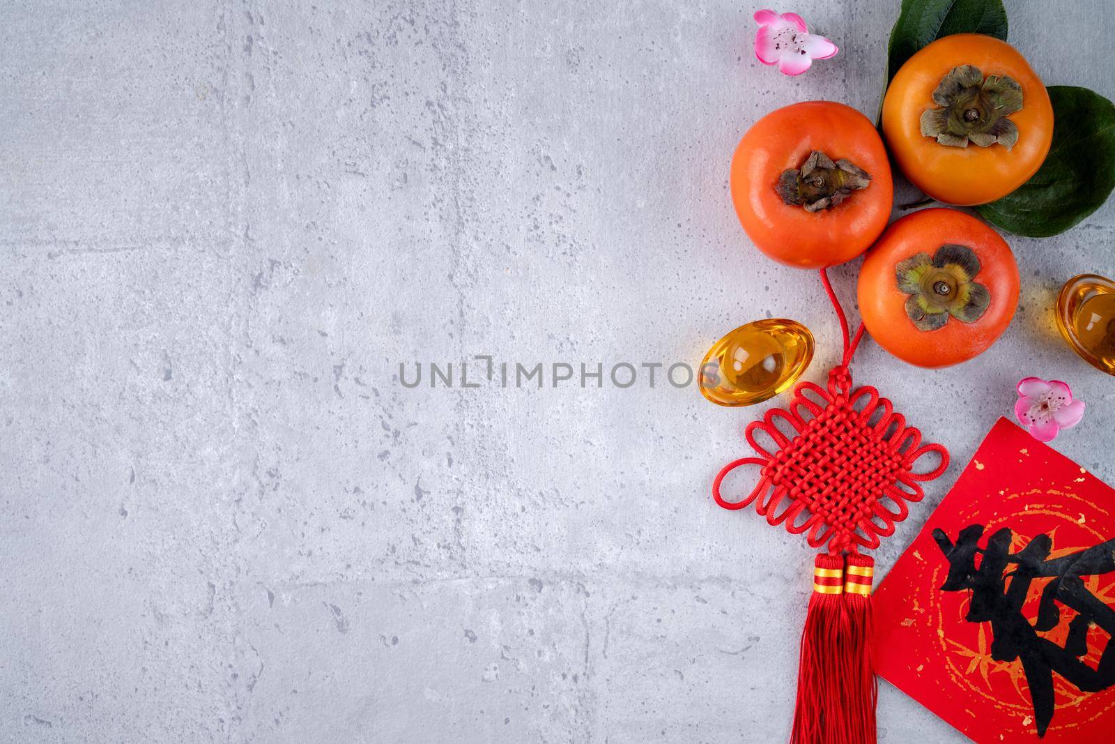 Top view of fresh sweet persimmons kaki with leaves on gray table background for Chinese lunar new year fruit design concept, the word means spring is coming.
