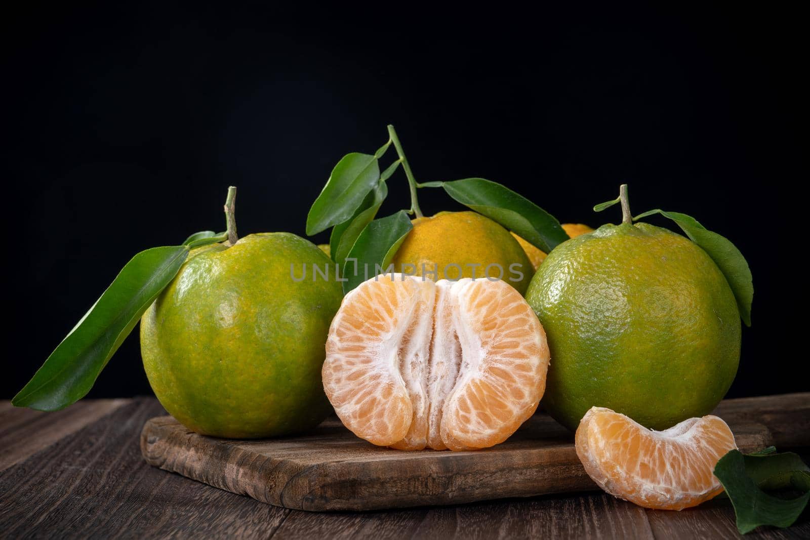 Fresh green tangerine mandarin orange with fresh leaves on dark wooden table background harvest concept.