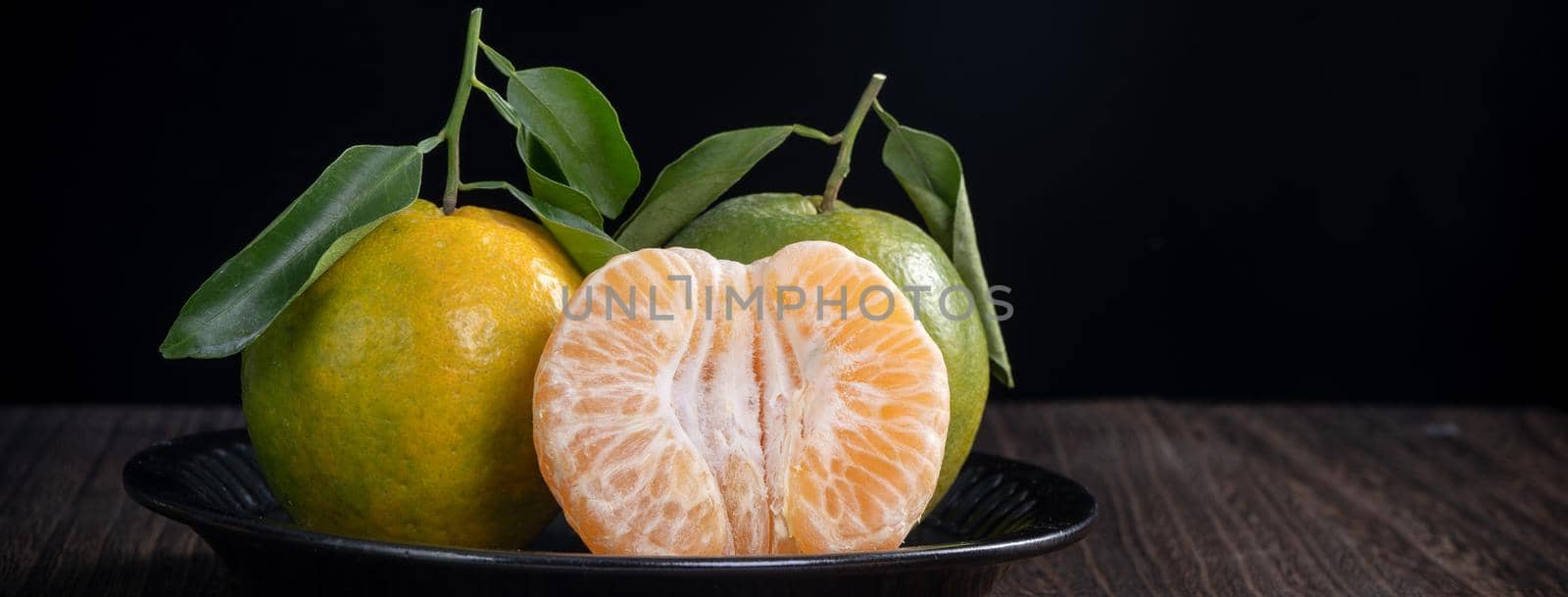 Fresh green tangerine mandarin orange with fresh leaves on dark wooden table background harvest concept.