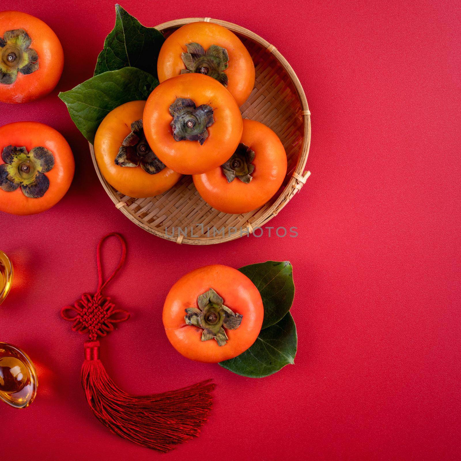 Top view of fresh sweet persimmons kaki with leaves on red table background for Chinese lunar new year fruit design concept, the word means spring is coming.