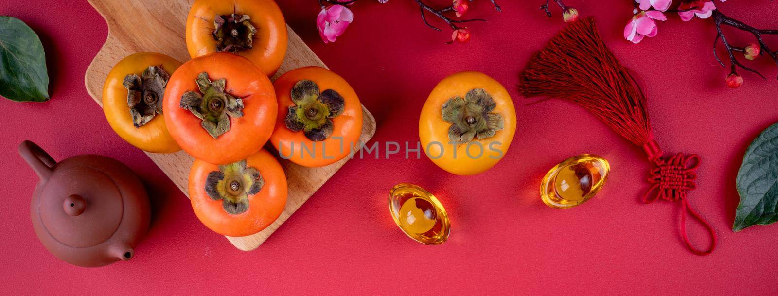 Top view of fresh sweet persimmons kaki with leaves on red table background for Chinese lunar new year fruit design concept, the word means spring is coming.