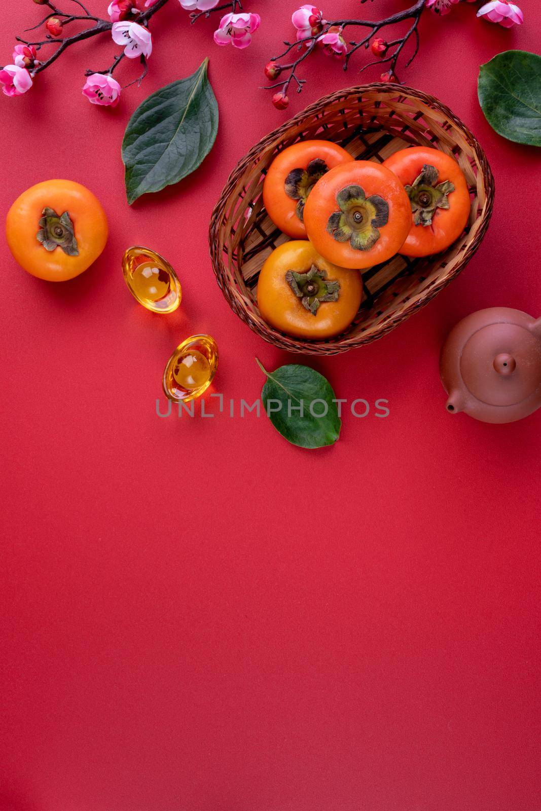 Top view of fresh sweet persimmons kaki with leaves on red table background for Chinese lunar new year fruit design concept, the word means spring is coming.