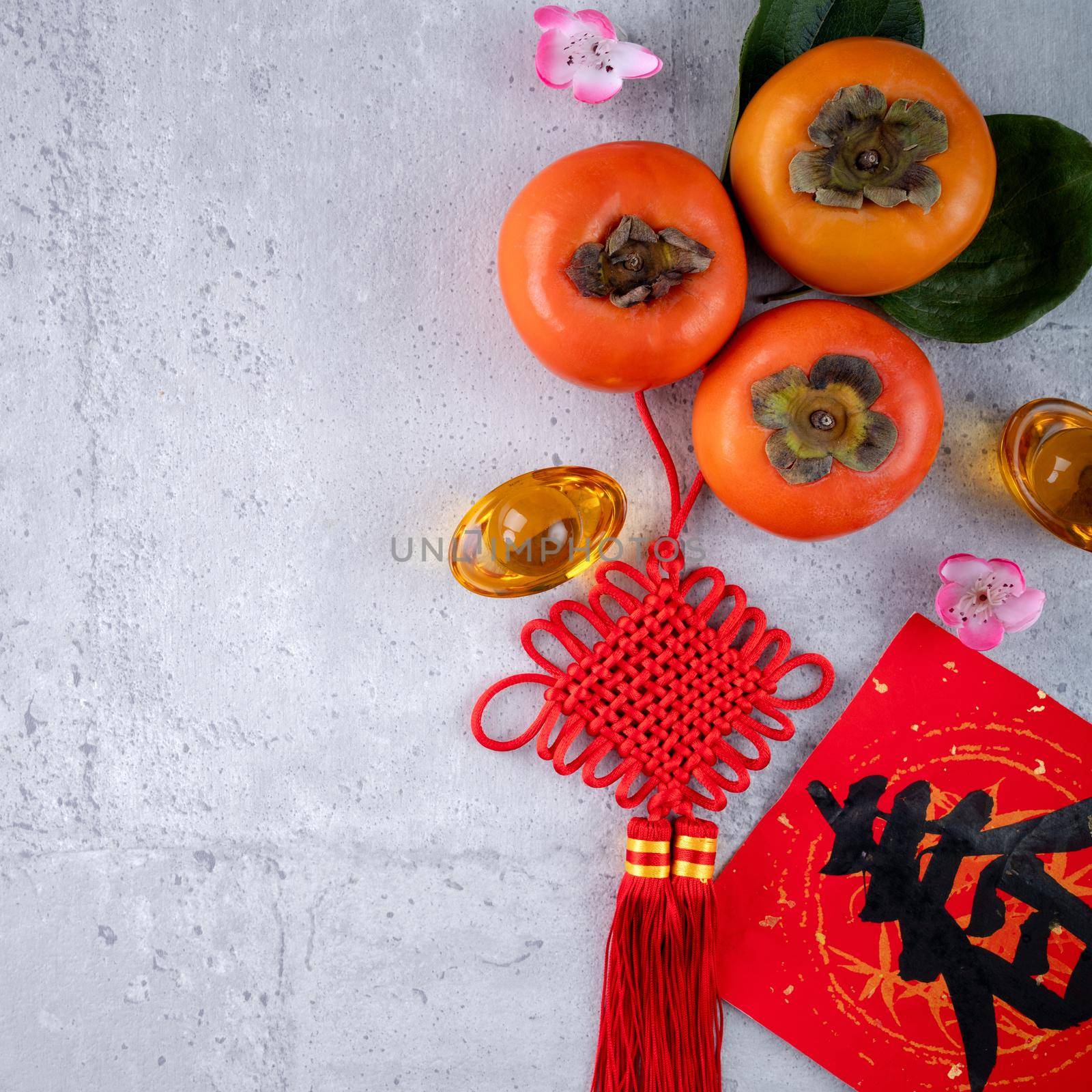 Top view of fresh sweet persimmons kaki with leaves on gray table background for Chinese lunar new year fruit design concept, the word means spring is coming.