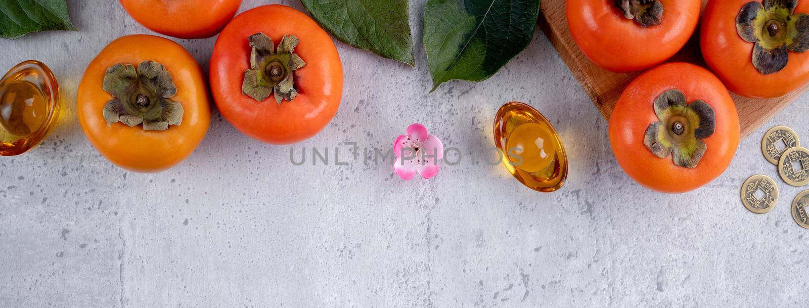 Top view of fresh sweet persimmons kaki with leaves on gray table background for Chinese lunar new year fruit design concept, the word means spring is coming.