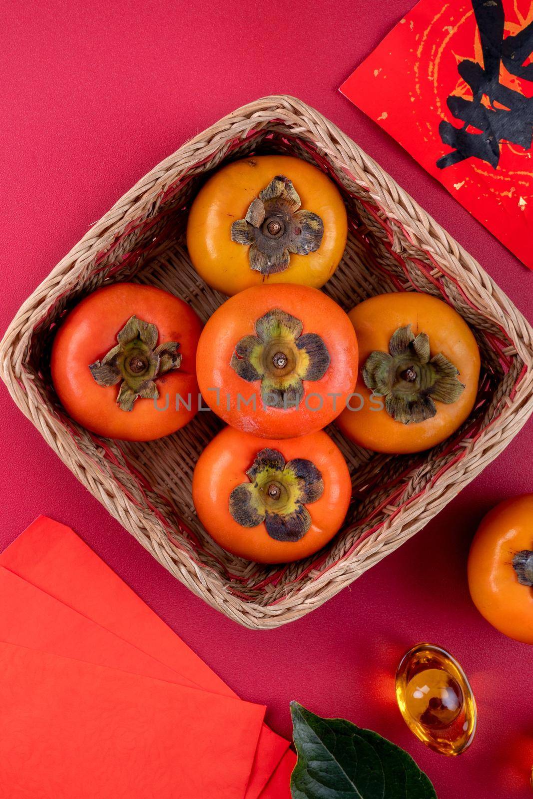 Top view of fresh sweet persimmons kaki with leaves on red table background for Chinese lunar new year fruit design concept, the word means spring is coming.