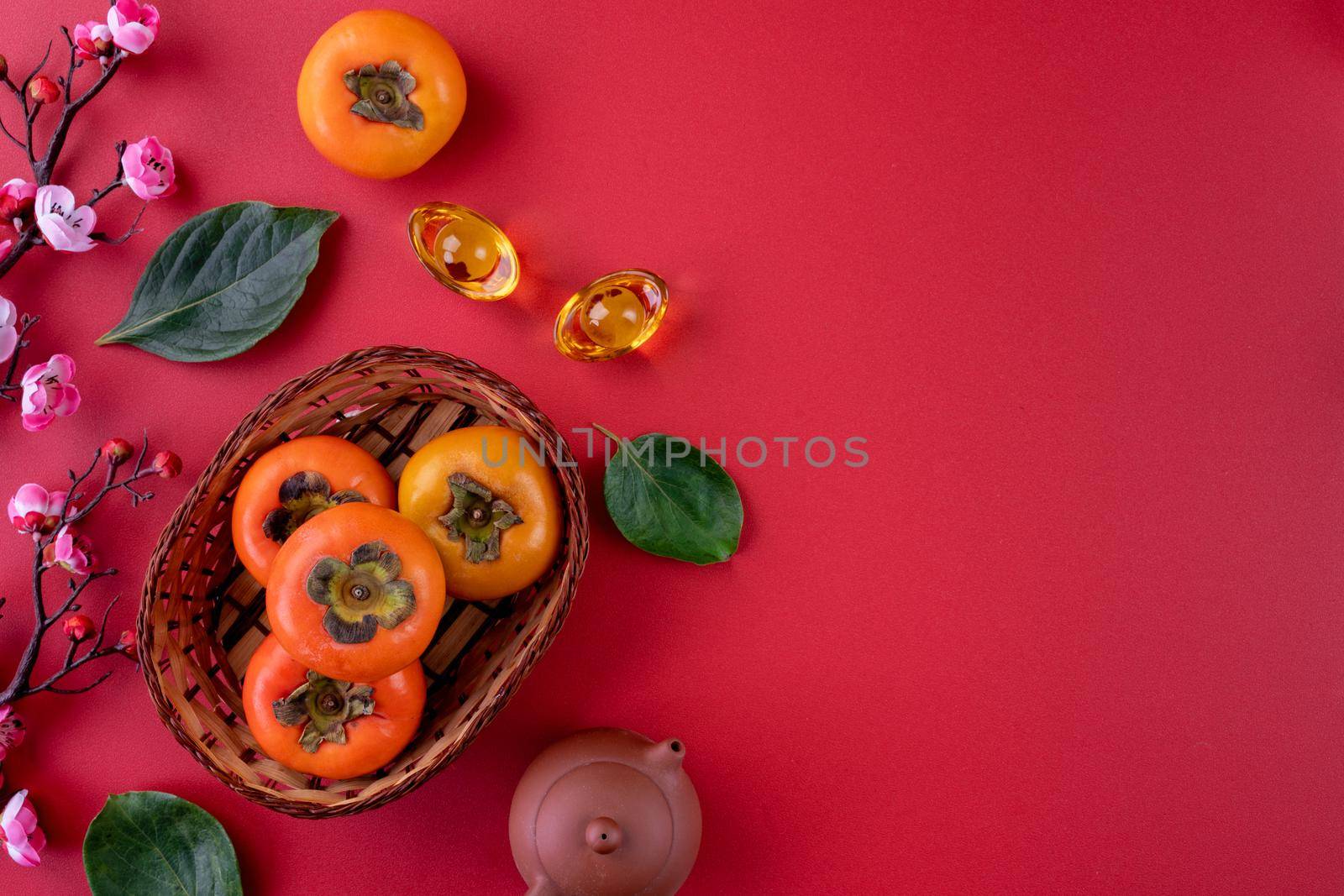 Top view of fresh sweet persimmons kaki with leaves on red table background for Chinese lunar new year fruit design concept, the word means spring is coming.