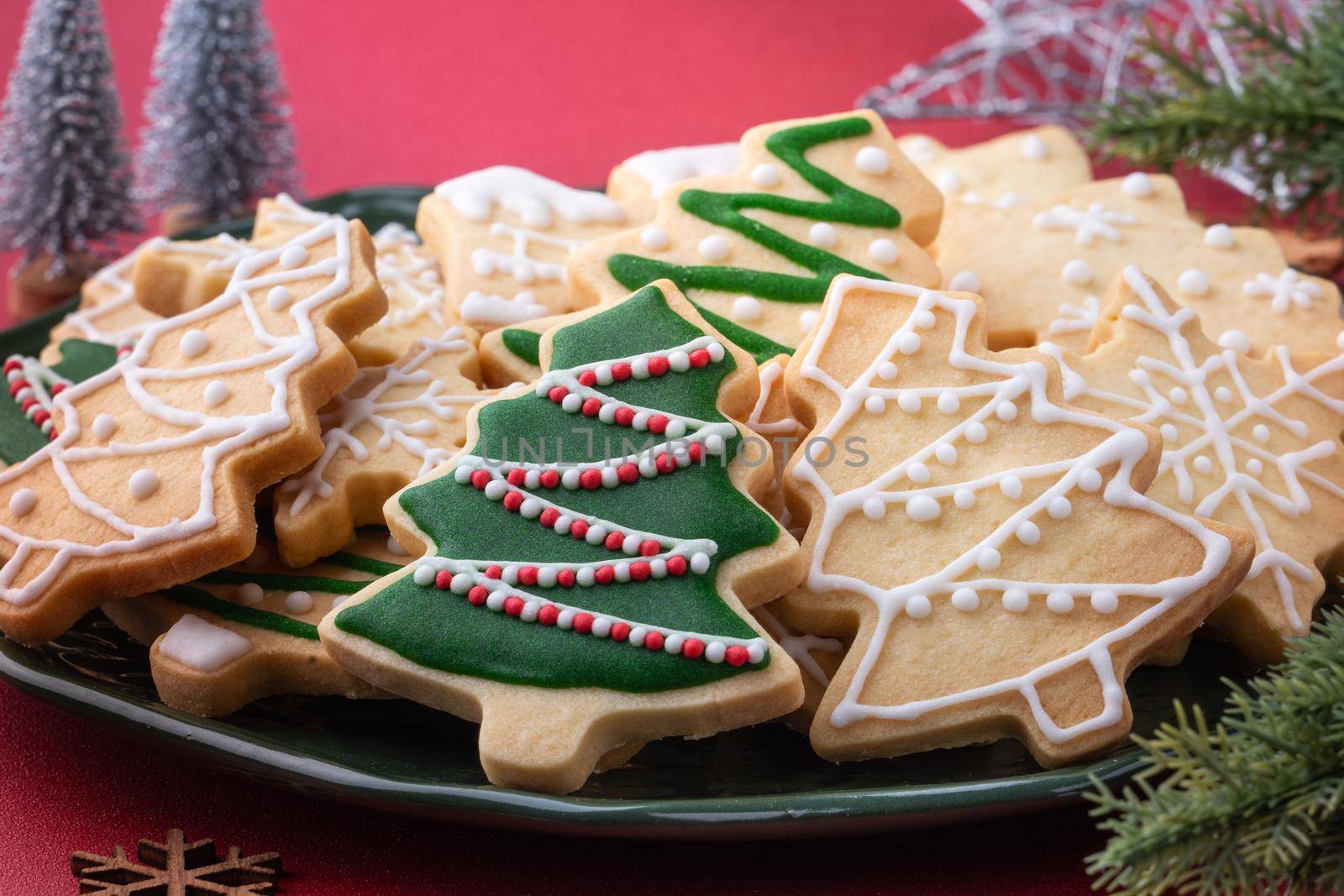 Close up of Christmas decorated sugar cookies in a plate on red table background.