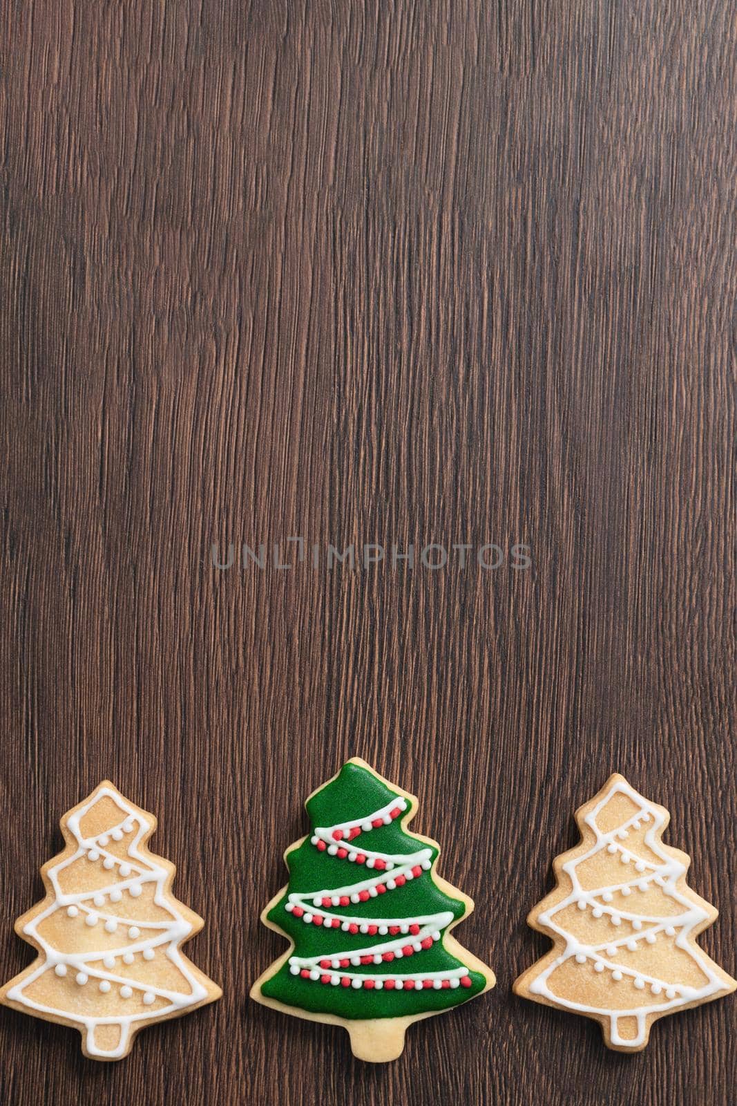 Close up of drawing gingerbread Christmas tree sugar cookie on wooden table background with green icing, concept of holiday celebration.