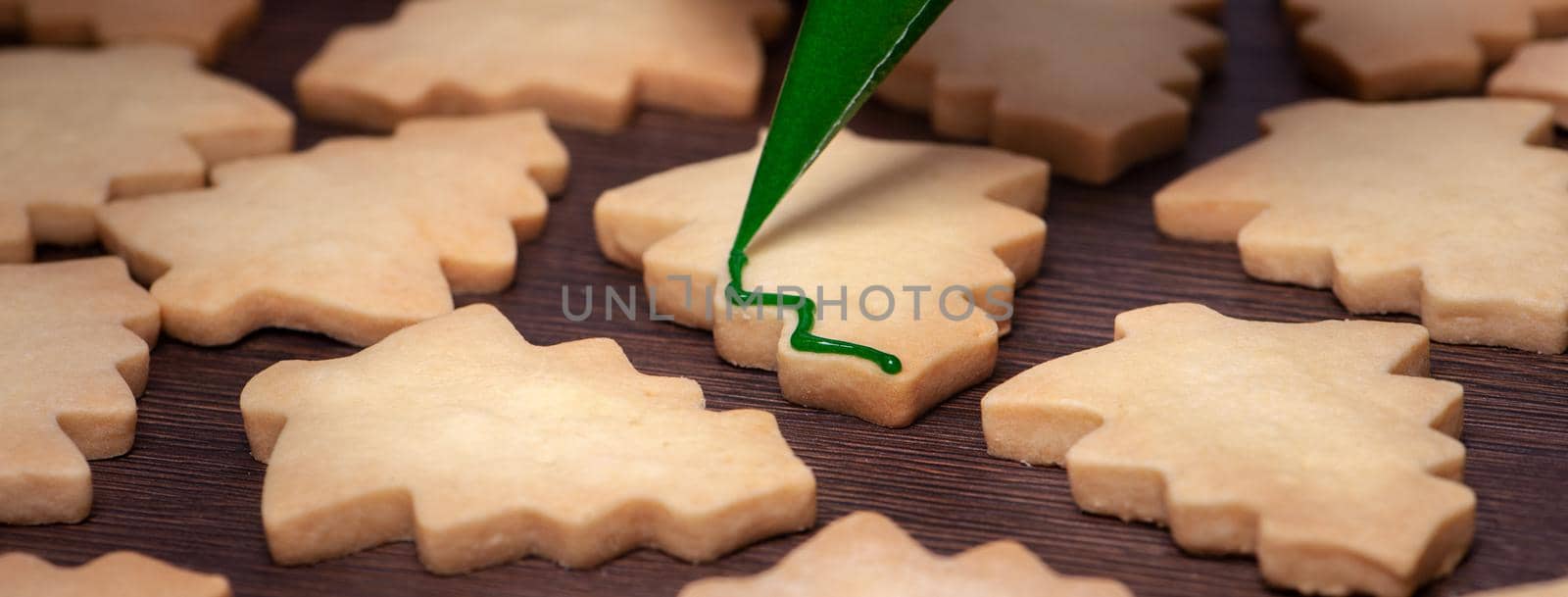 Close up of drawing gingerbread Christmas tree sugar cookie on wooden table background with green icing, concept of holiday celebration.