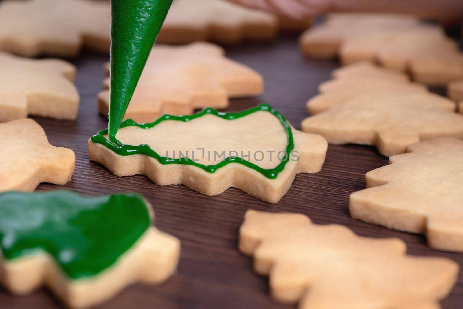 Close up of drawing gingerbread Christmas tree sugar cookie on wooden table background with green icing, concept of holiday celebration.