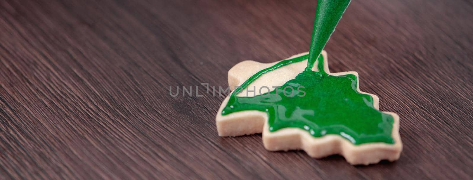 Close up of drawing gingerbread Christmas tree sugar cookie on wooden table background with green icing, concept of holiday celebration.