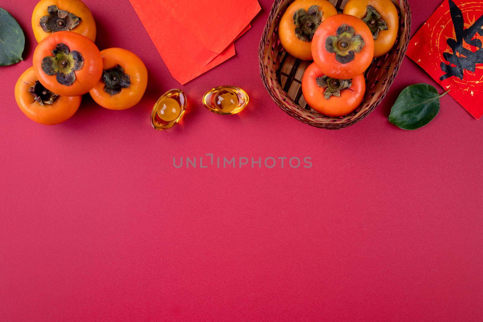 Top view of fresh sweet persimmons kaki with leaves on red table background for Chinese lunar new year fruit design concept, the word means spring is coming.