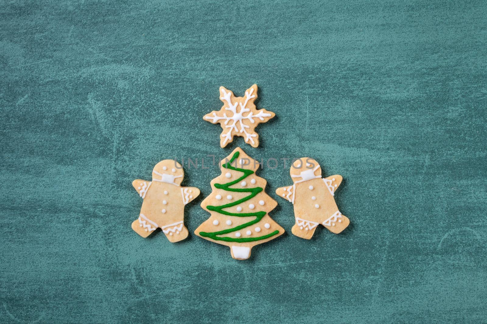 Top view of Christmas tree and snowflake cooikes with gingerbread man wearing mask on green table background.