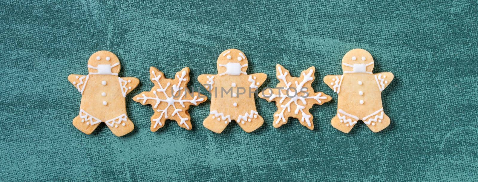 Top view of Christmas tree and snowflake cooikes with gingerbread man wearing mask on green table background.