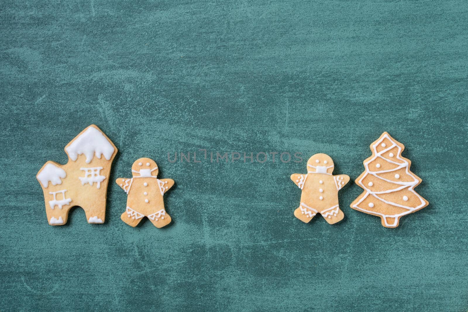 Top view of Christmas tree and snowflake cooikes with gingerbread man wearing mask on green table background.