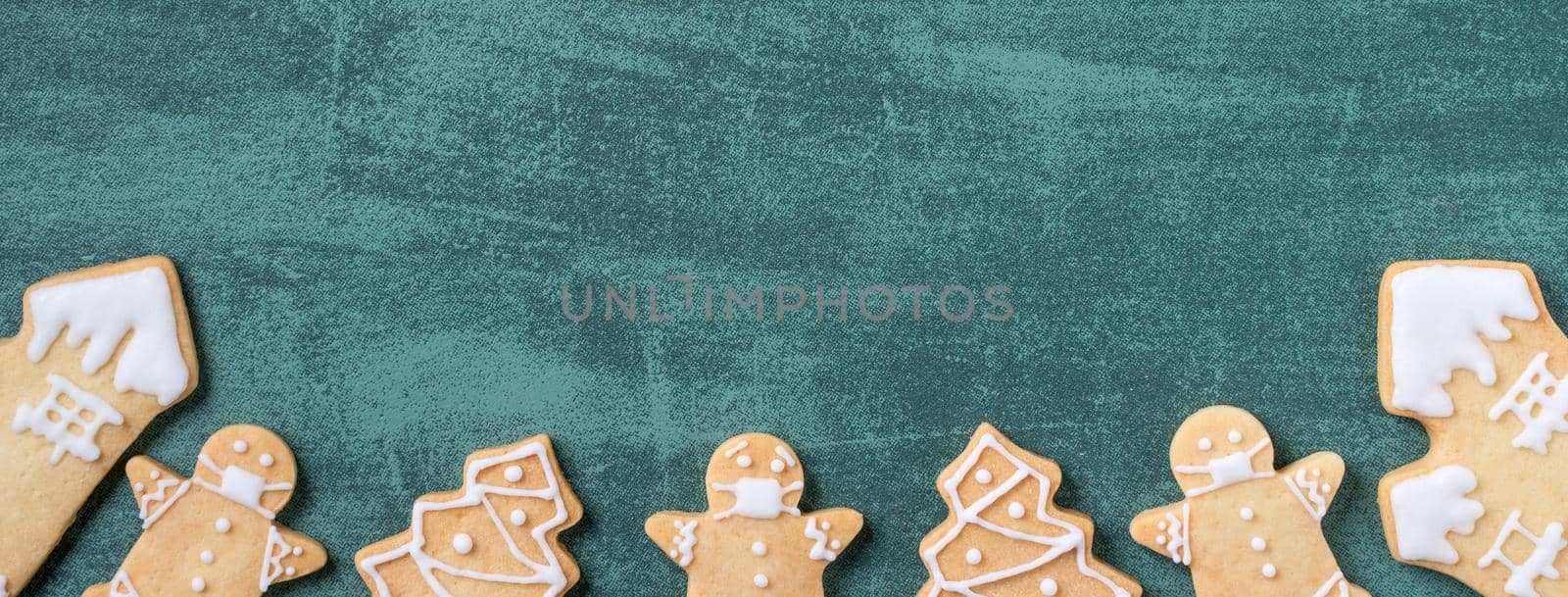 Top view of Christmas tree and snowflake cooikes with gingerbread man wearing mask on green table background.