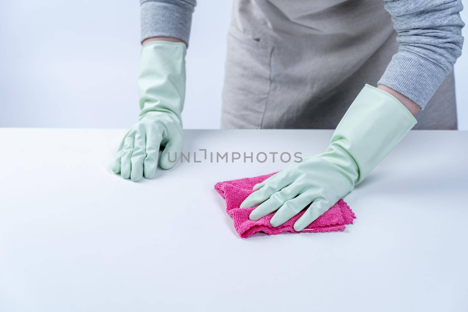 Young woman housekeeper in apron is cleaning, wiping down table surface with wet rag, spraying bottle cleaner to prevent disease spreading.