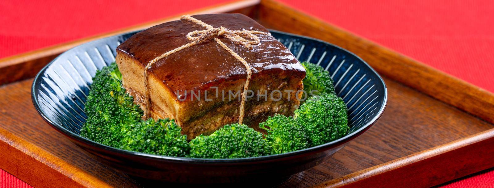Dong Po Rou (Dongpo pork meat) in a beautiful blue plate with green broccoli vegetable, traditional festive food for Chinese new year cuisine meal, close up.