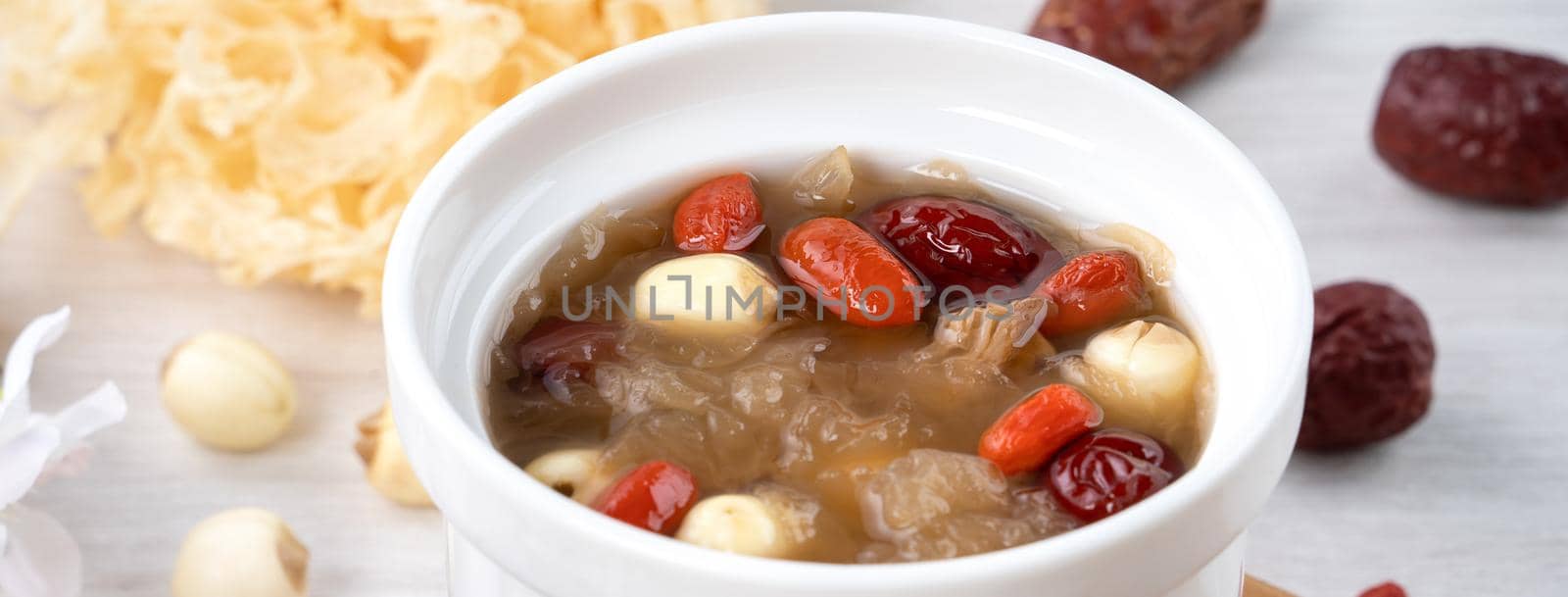 Close up of traditional Chinese sweet snow white fungus soup with lotus seed, red dates (jujube) and wolfberry (goji, gojiberry) on white background.