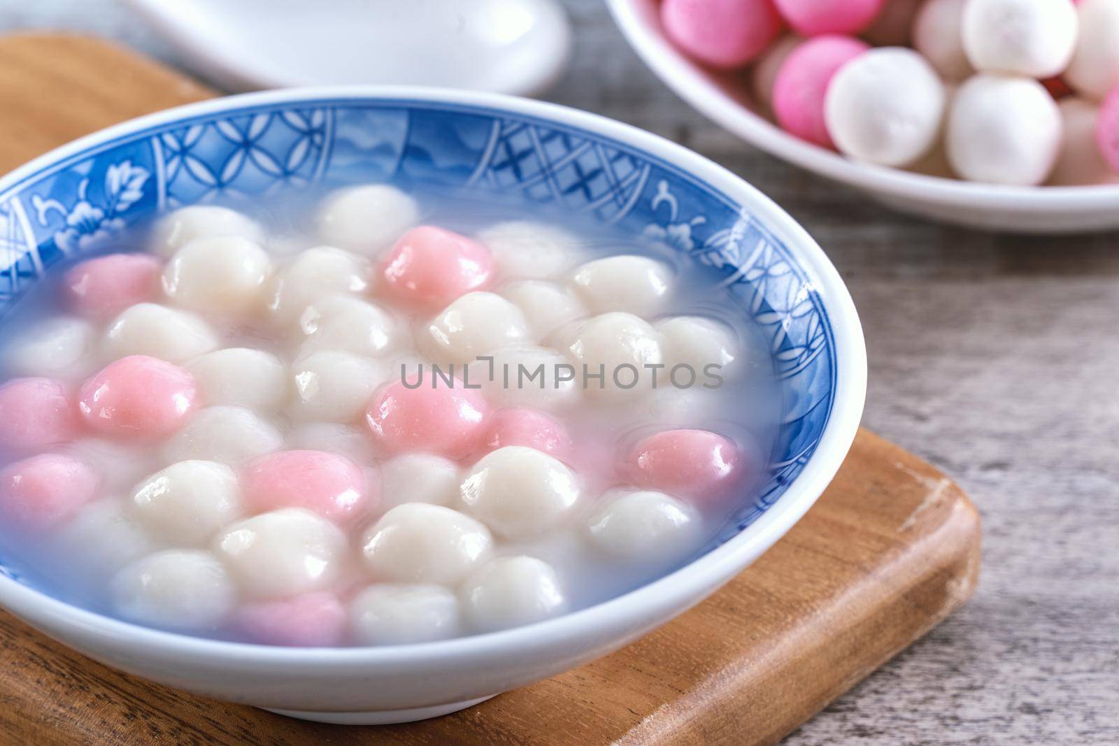 Close up of red and white tangyuan (tang yuan, glutinous rice dumpling balls) in blue bowl on wooden background for Winter solstice festival food.