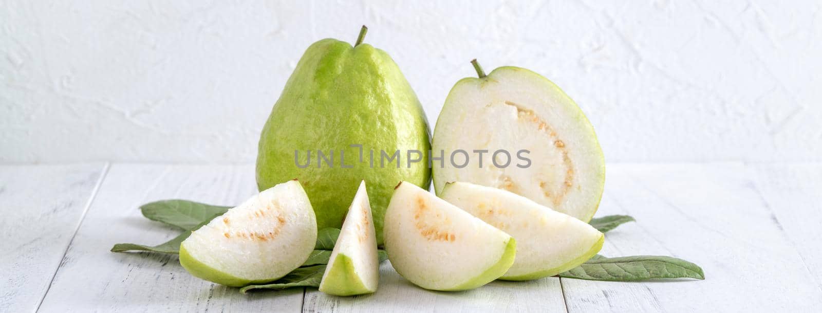 Delicious beautiful guava set with fresh leaves isolated on bright white wooden table background, close up.