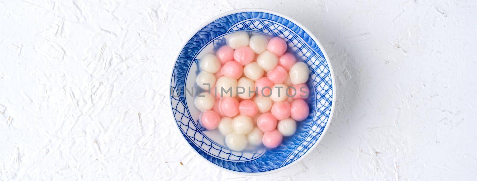 Top view of red and white tangyuan (tang yuan, glutinous rice dumpling balls) in blue bowl on white background for Winter solstice festival food.