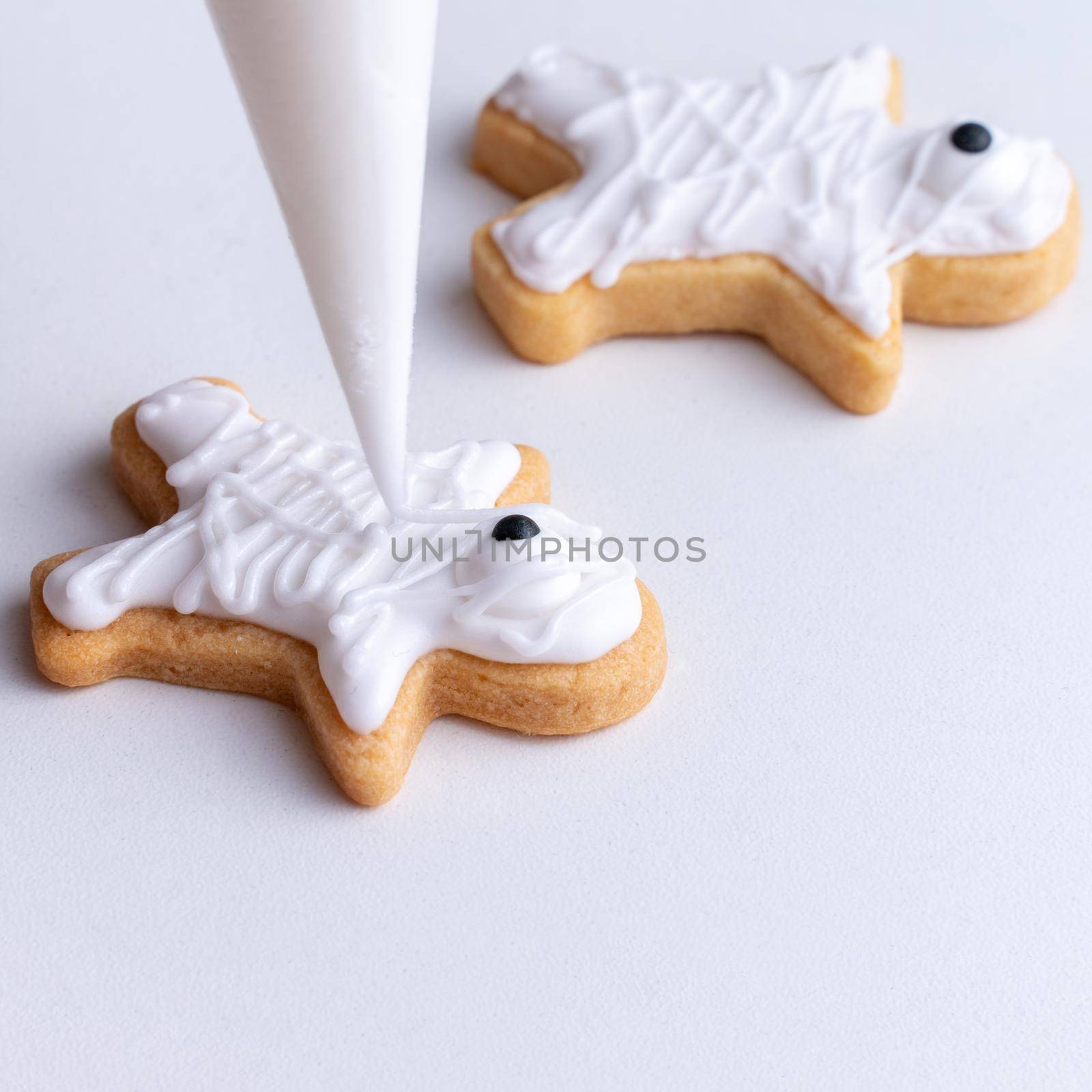 Close up of decorating cute Halloween gingerbread cookies with frosting icing cream topping bag.