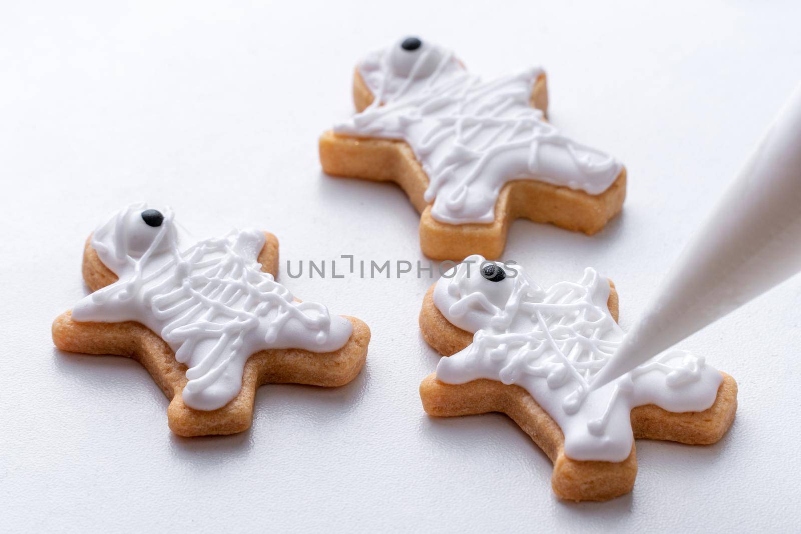 Close up of decorating cute Halloween gingerbread cookies with frosting icing cream topping bag.