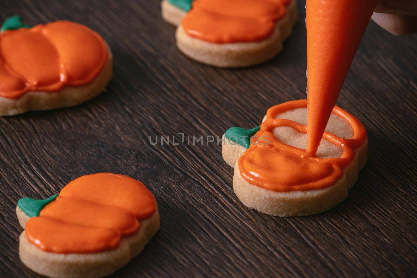 Close up of decorating cute Halloween pumpkin gingerbread cookies with frosting icing cream topping bag.