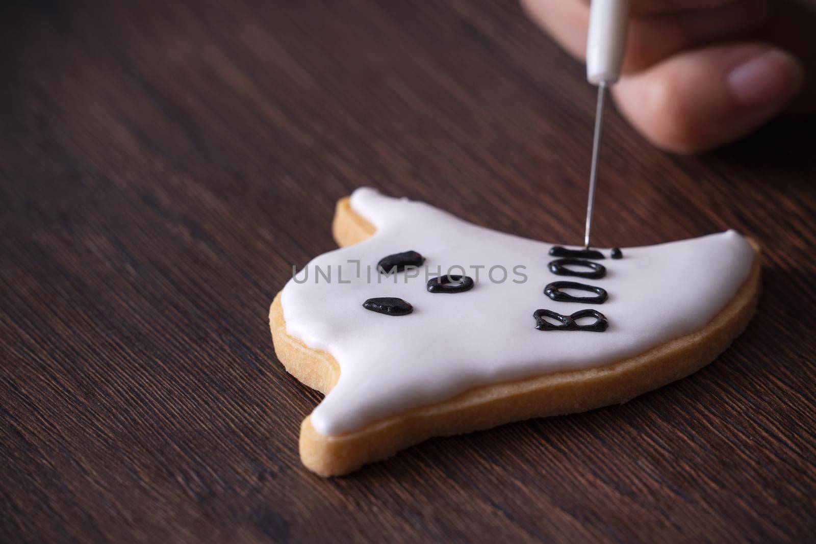 Close up of decorating cute Halloween ghost gingerbread cookies with frosting icing cream topping bag.