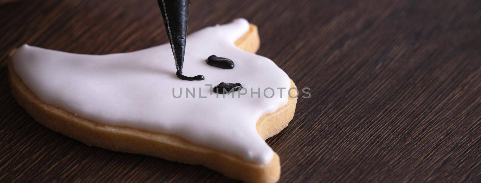 Close up of decorating cute Halloween ghost gingerbread cookies with frosting icing cream topping bag.