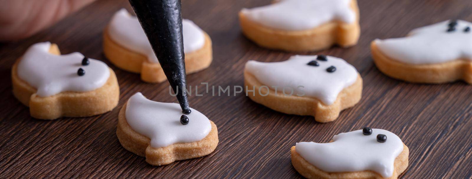 Close up of decorating cute Halloween ghost gingerbread cookies with frosting icing cream topping bag.
