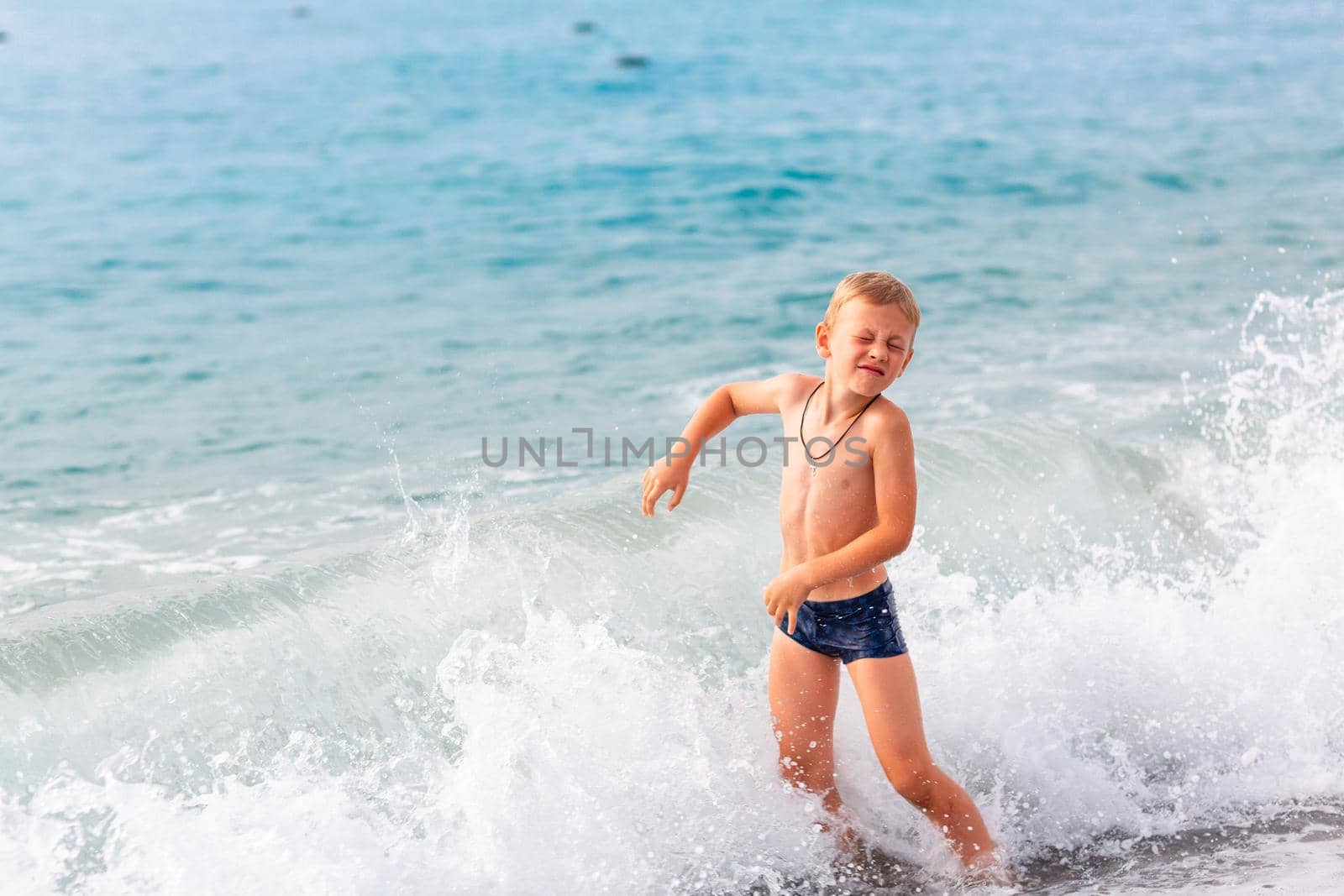 Happy active little boy having fun in the spalshes in the waves at the seaside