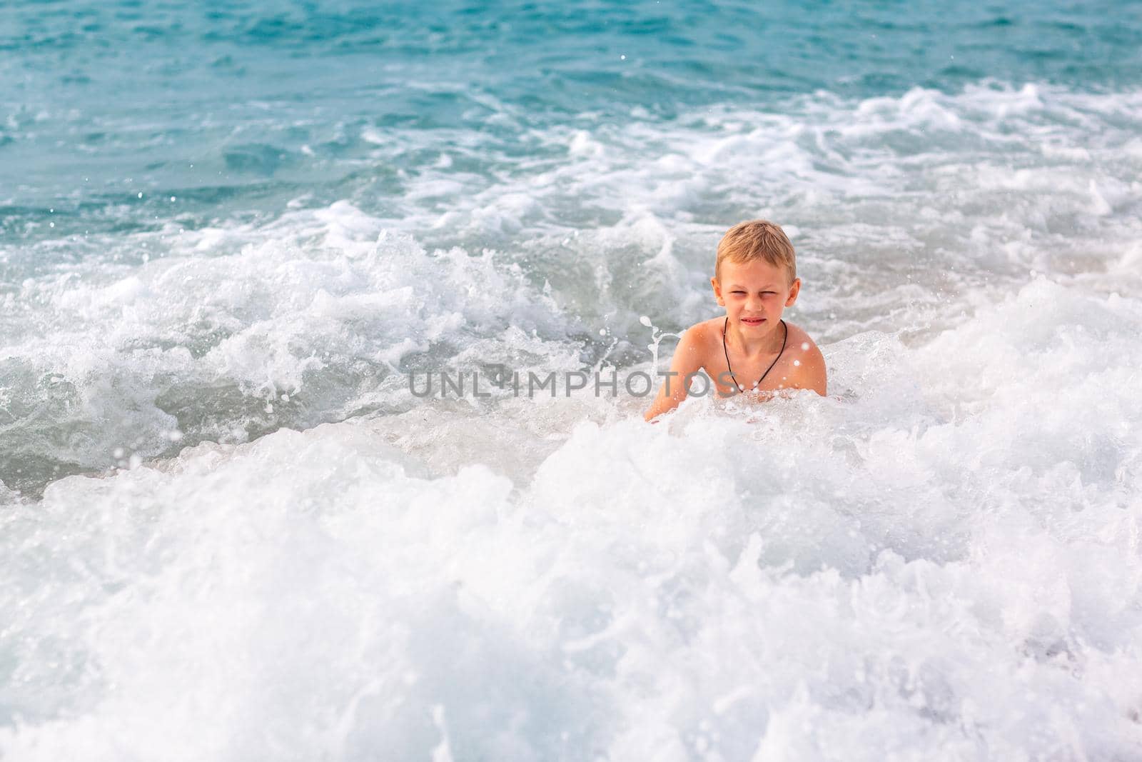 Happy active little boy having fun in the spalshes in the waves at the seaside