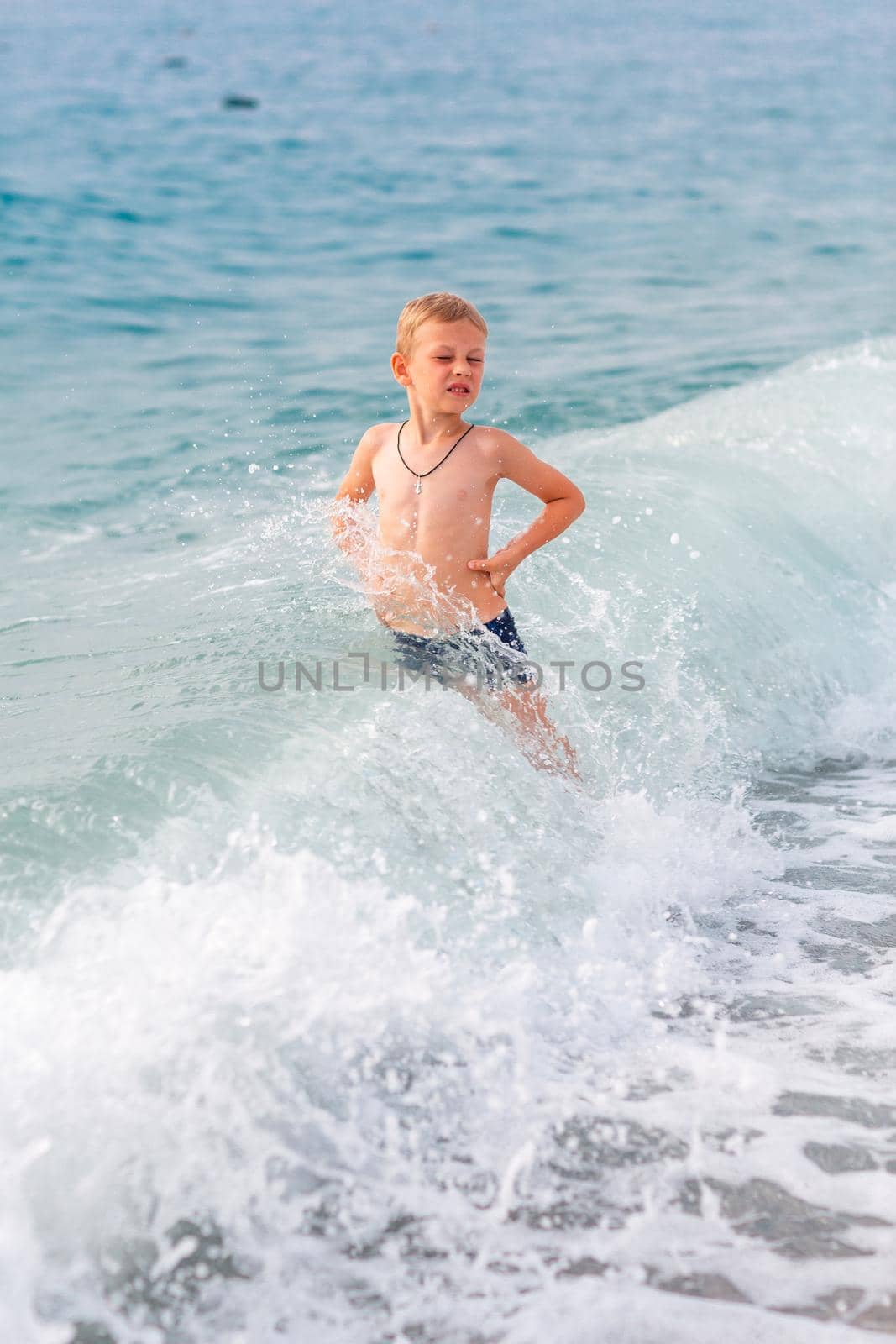 Happy active little boy having fun in the spalshes in the waves at the seaside