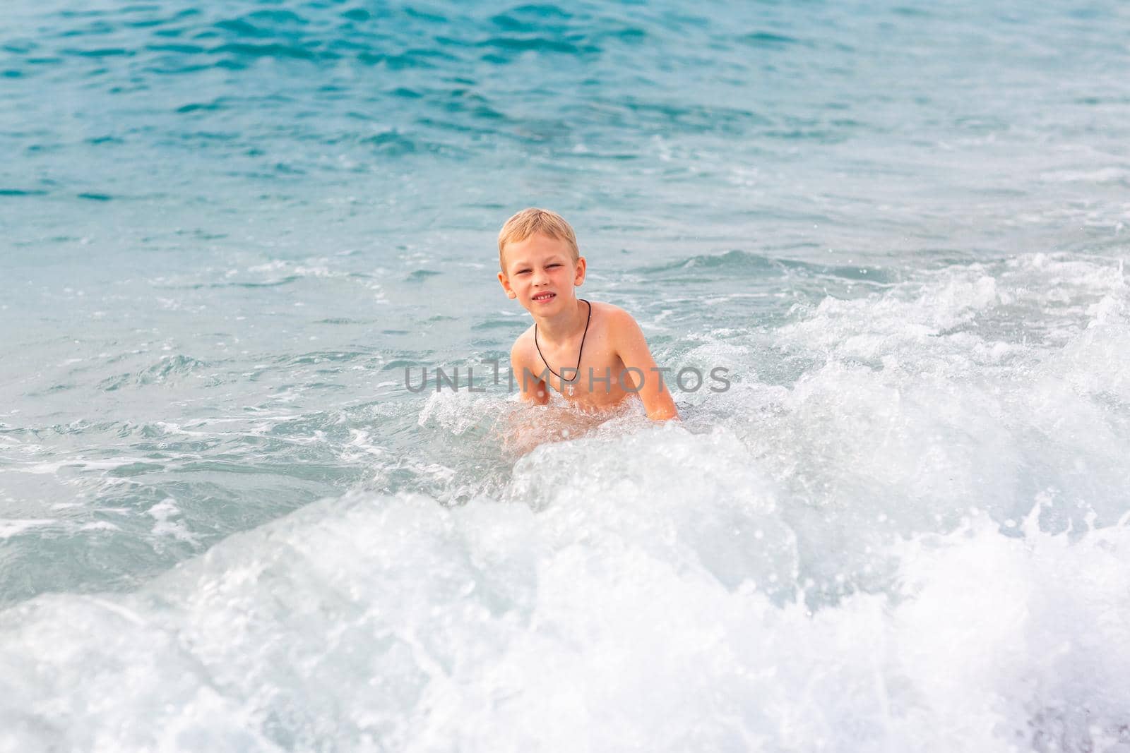 Happy active little boy having fun in the spalshes in the waves at the seaside