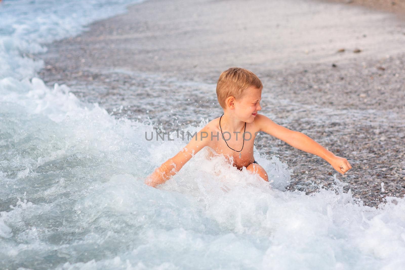 Happy active little boy having fun in the spalshes in the waves at the seaside