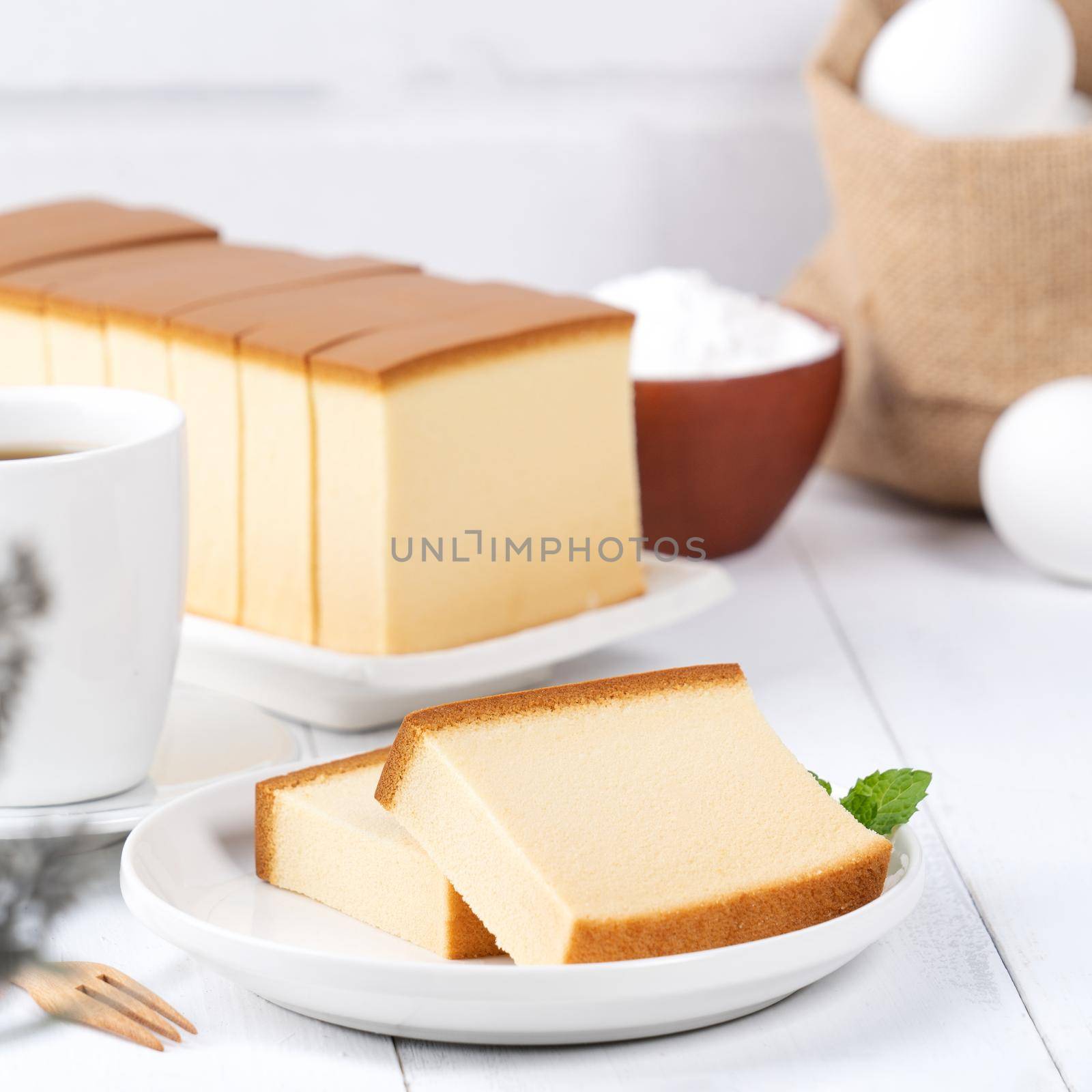 Castella (kasutera) - Beautiful delicious Japanese sliced sponge cake food on white plate over rustic white wooden table, close up, copy space design concept.