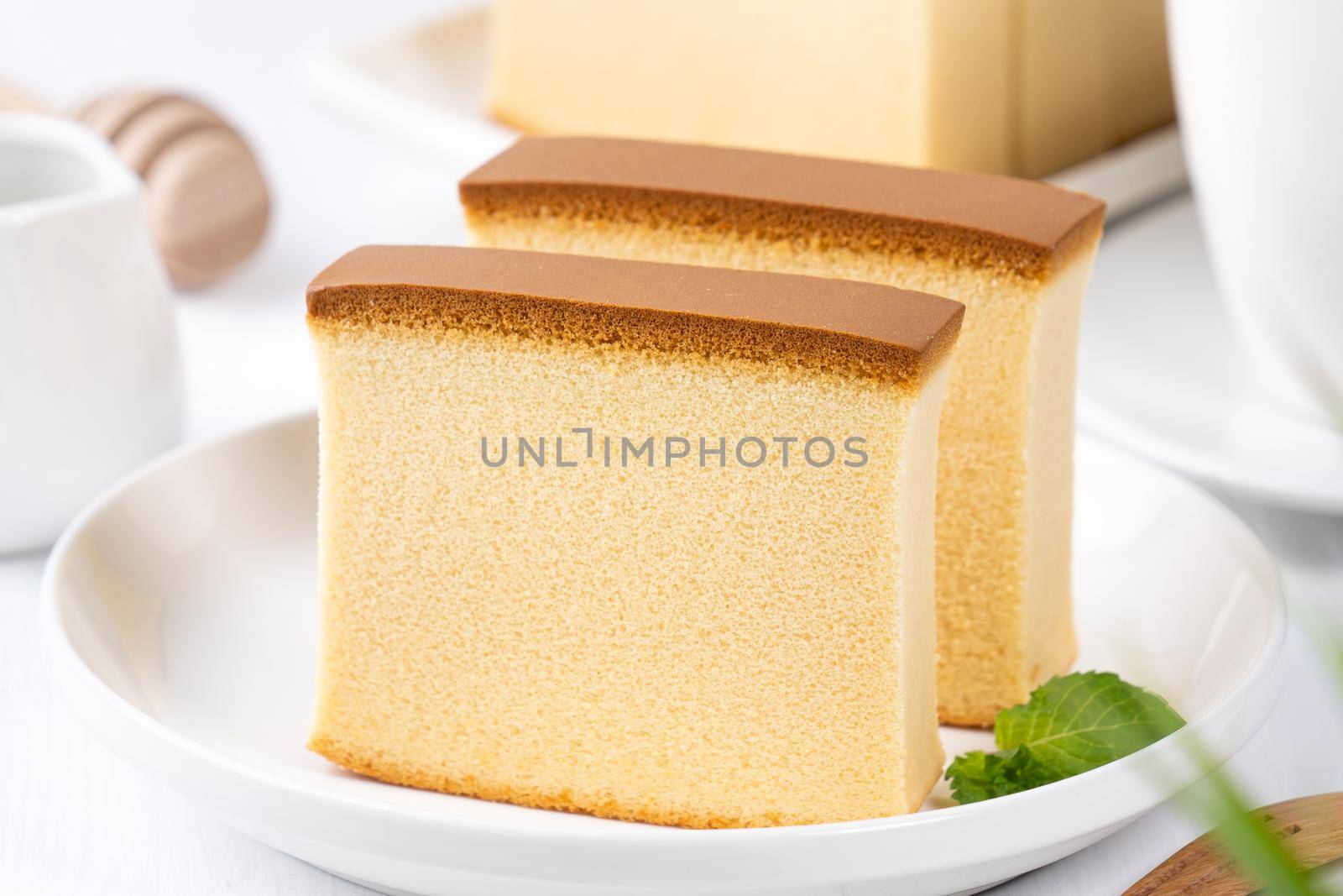 Castella (kasutera) - Beautiful delicious Japanese sliced sponge cake food on white plate over rustic white wooden table, close up, copy space design concept.