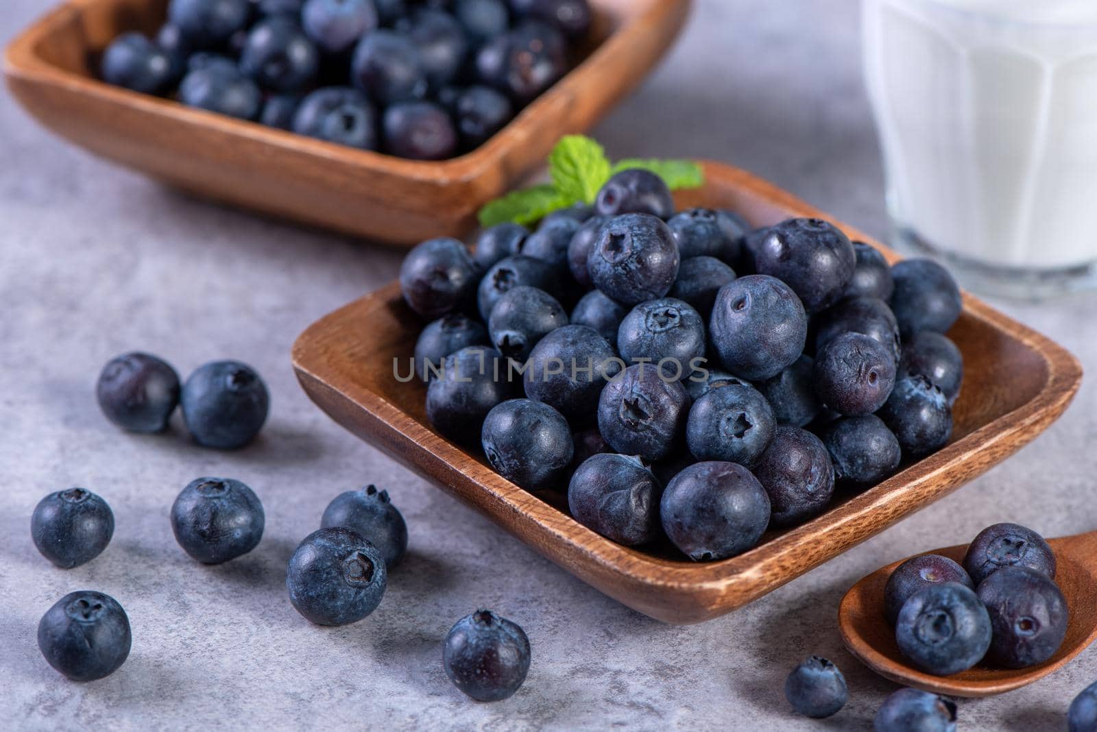 Pile of blueberry fruit in a bowl plate on a tray over gray cement concrete background, close up, healthy eating design concept.