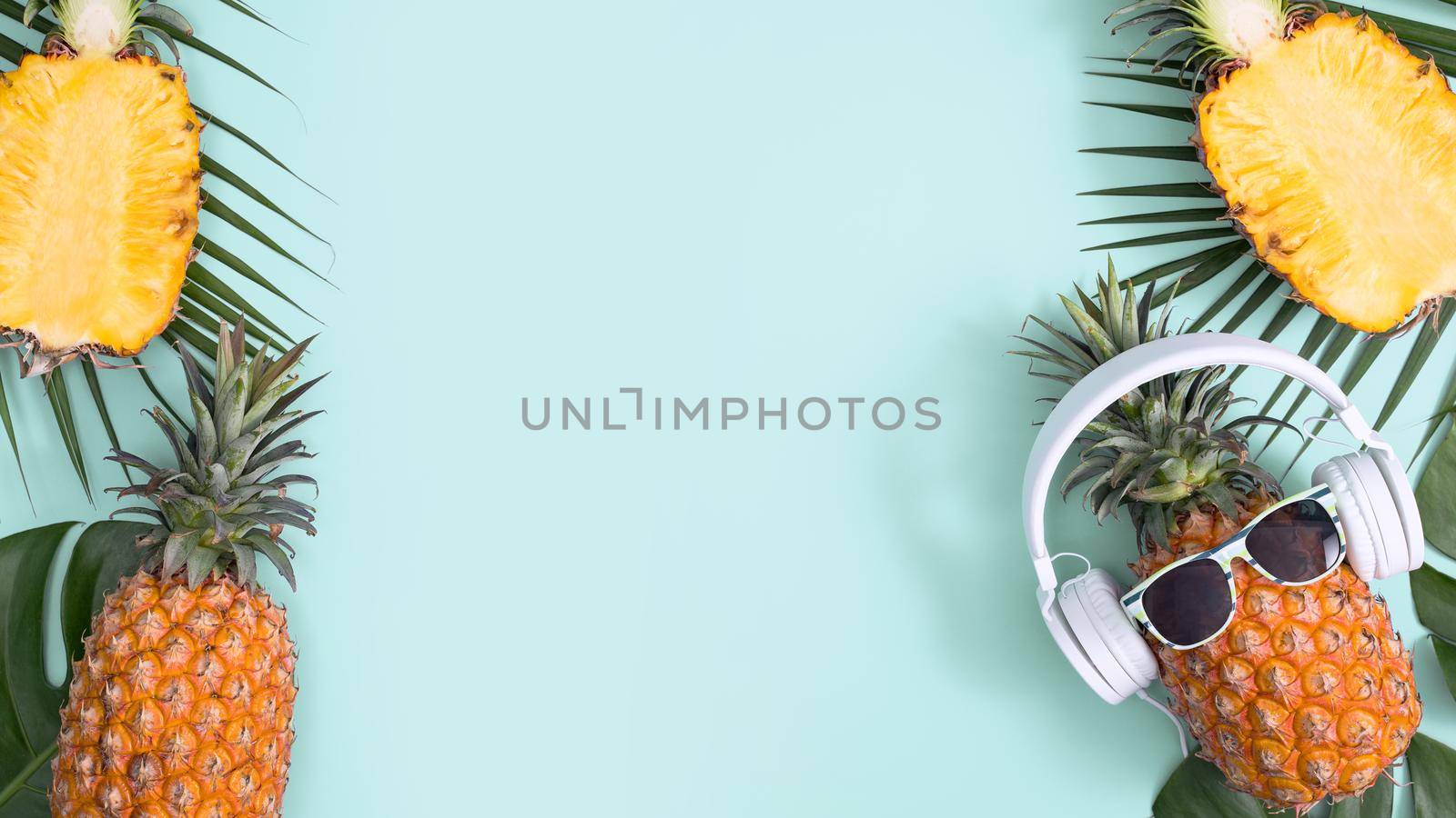 Funny pineapple wearing white headphone, concept of listening music, isolated on colored background with tropical palm leaves, top view, flat lay design.